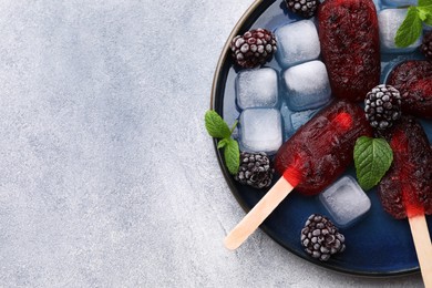 Photo of Plate of tasty blackberry ice pops and space for text on light grey table, top view. Fruit popsicle
