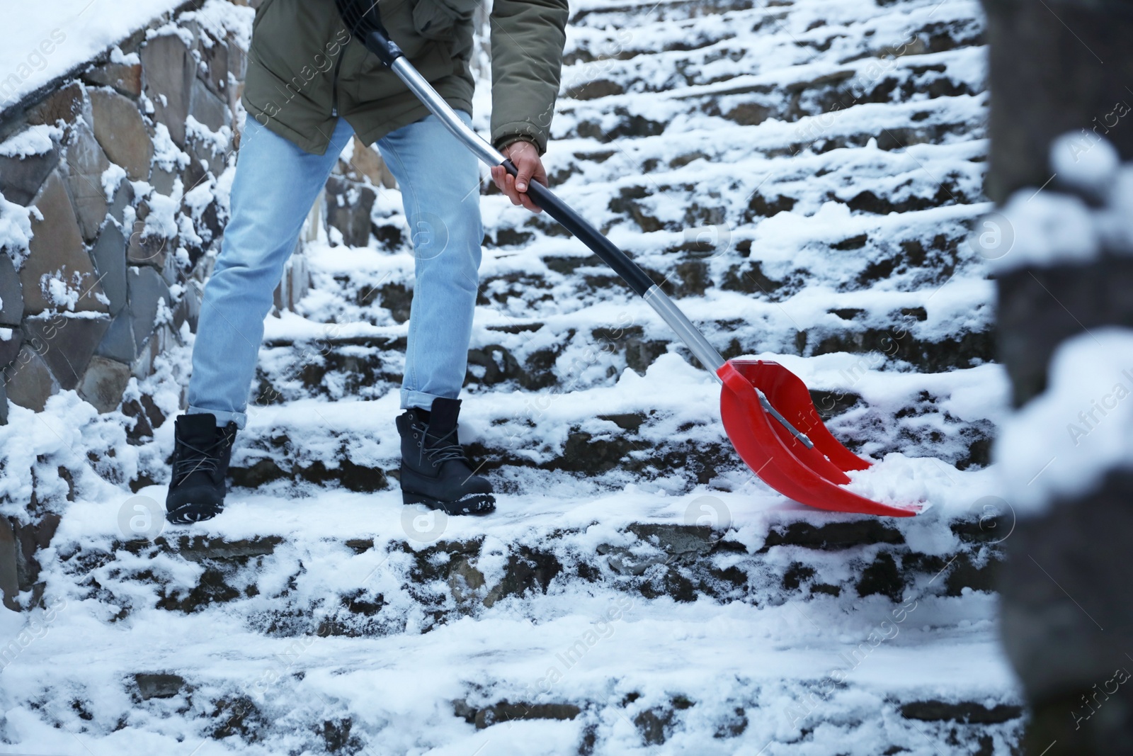 Photo of Man cleaning stairs from snow with shovel outdoors on winter day, closeup