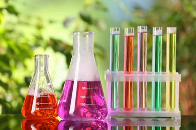 Laboratory glassware and test tubes with colorful liquids on glass table outdoors. Chemical reaction
