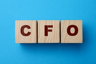 Photo of Abbreviation CFO of wooden cubes on blue background, flat lay. Financial management