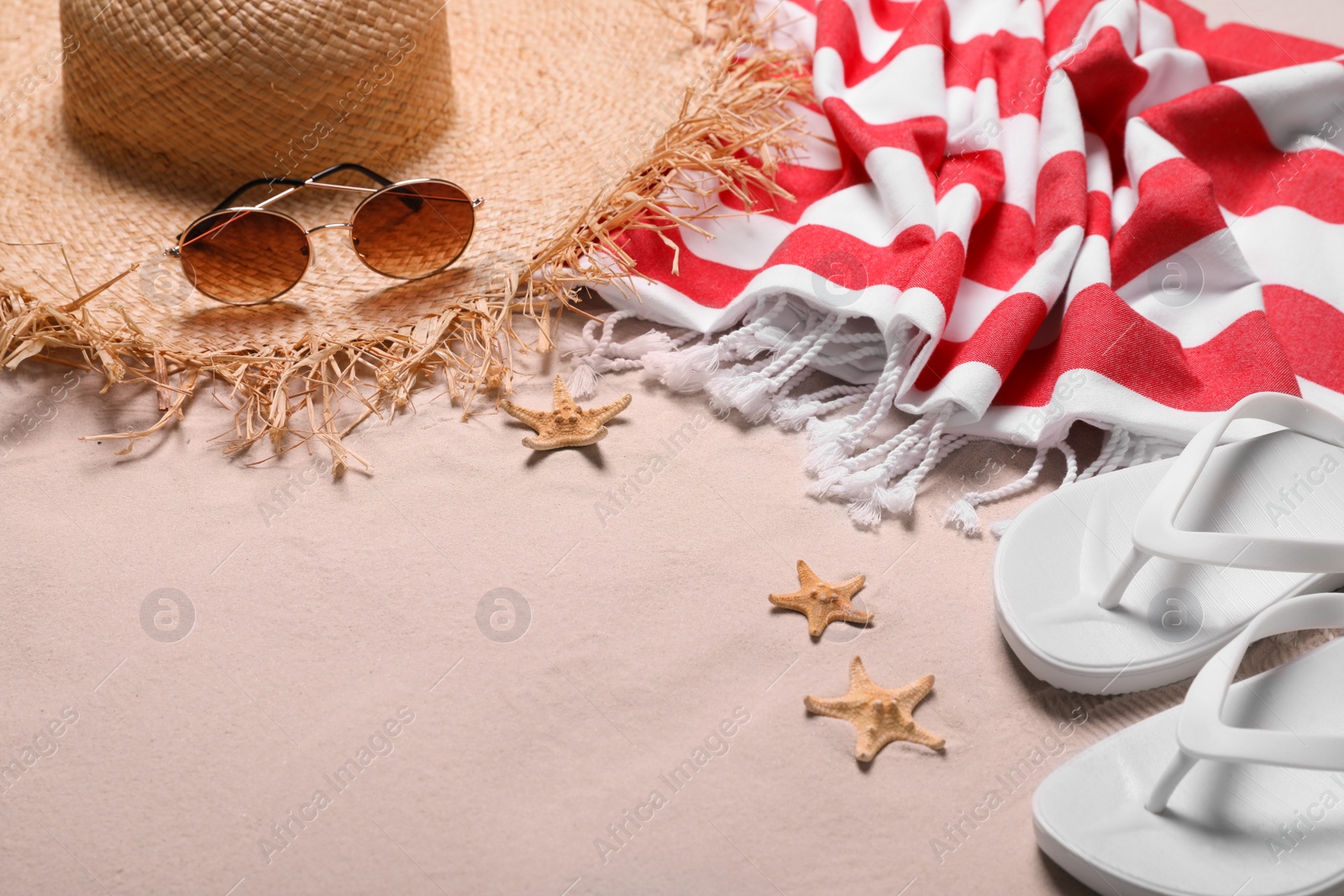 Photo of Beach towel, hat, sunglasses, starfishes and flip flops on sand