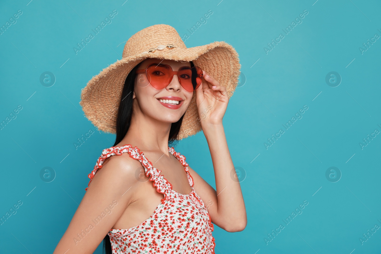 Photo of Beautiful young woman with straw hat and heart shaped sunglasses on light blue background. Space for text