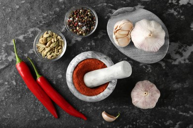 Photo of Mortar with red curry paste and ingredients on black textured table, flat lay