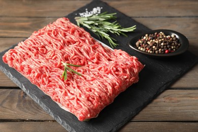 Photo of Raw ground meat, spices and rosemary on wooden table, closeup