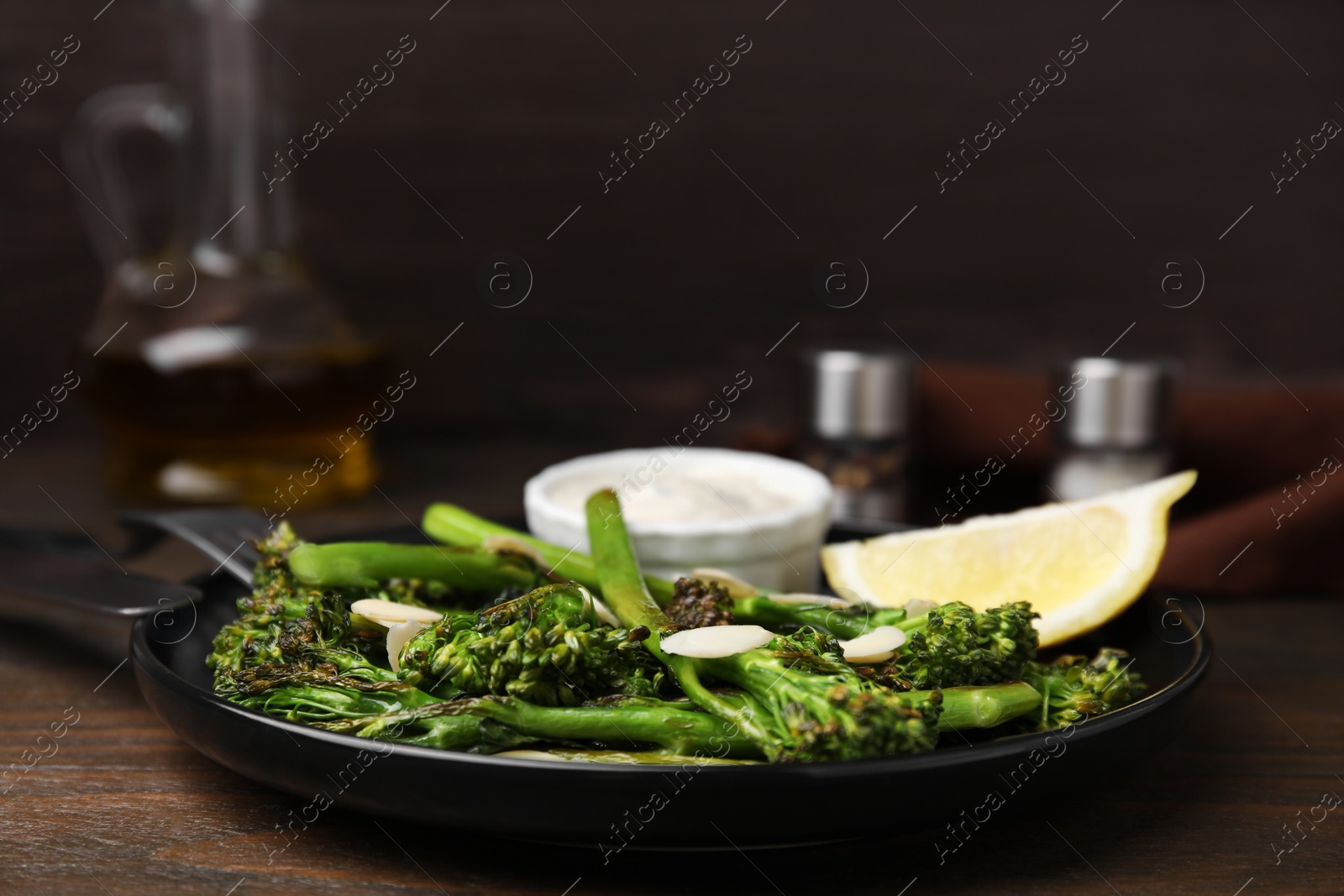 Photo of Tasty cooked broccolini with almonds, lemon and sauce on wooden table, closeup