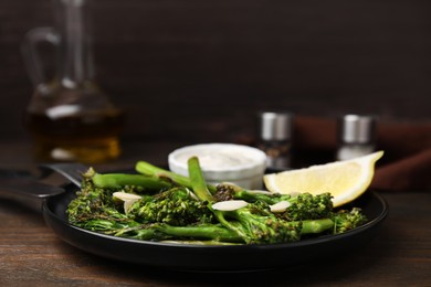 Tasty cooked broccolini with almonds, lemon and sauce on wooden table, closeup