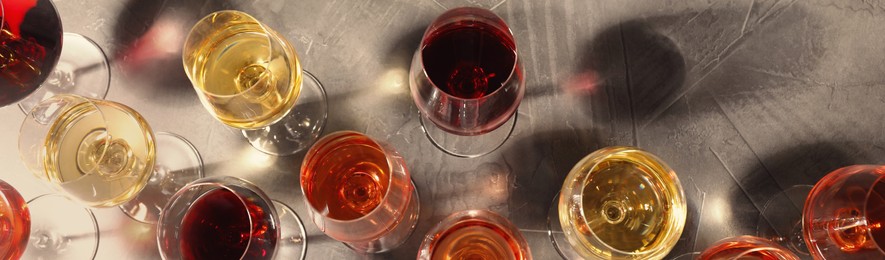 Glasses with different wines on grey table, flat lay. Banner design