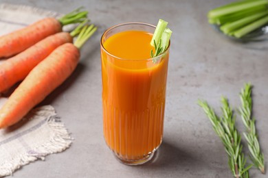 Photo of Glass of tasty carrot juice with celery sticks on grey table, closeup