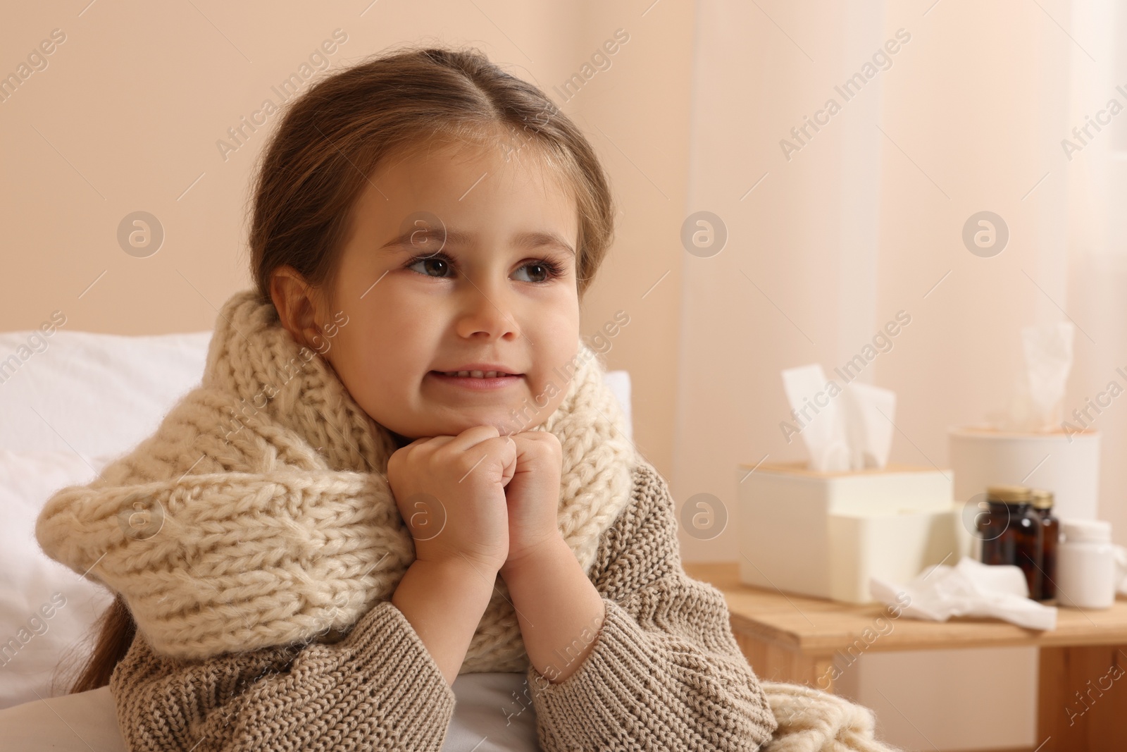 Photo of Sick girl with scarf around neck on bed in room