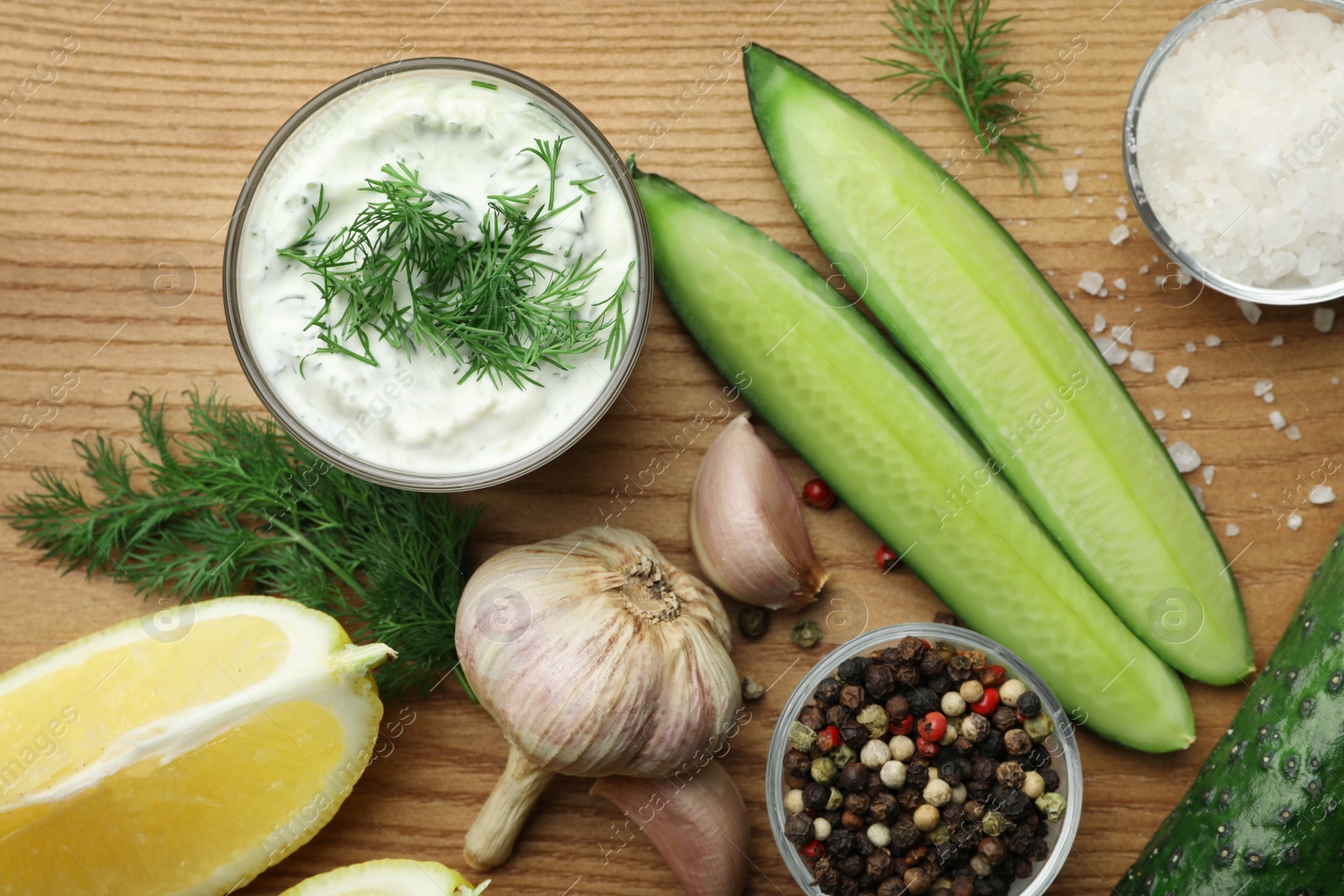 Photo of Tzatziki cucumber sauce with ingredients on wooden background, flat lay