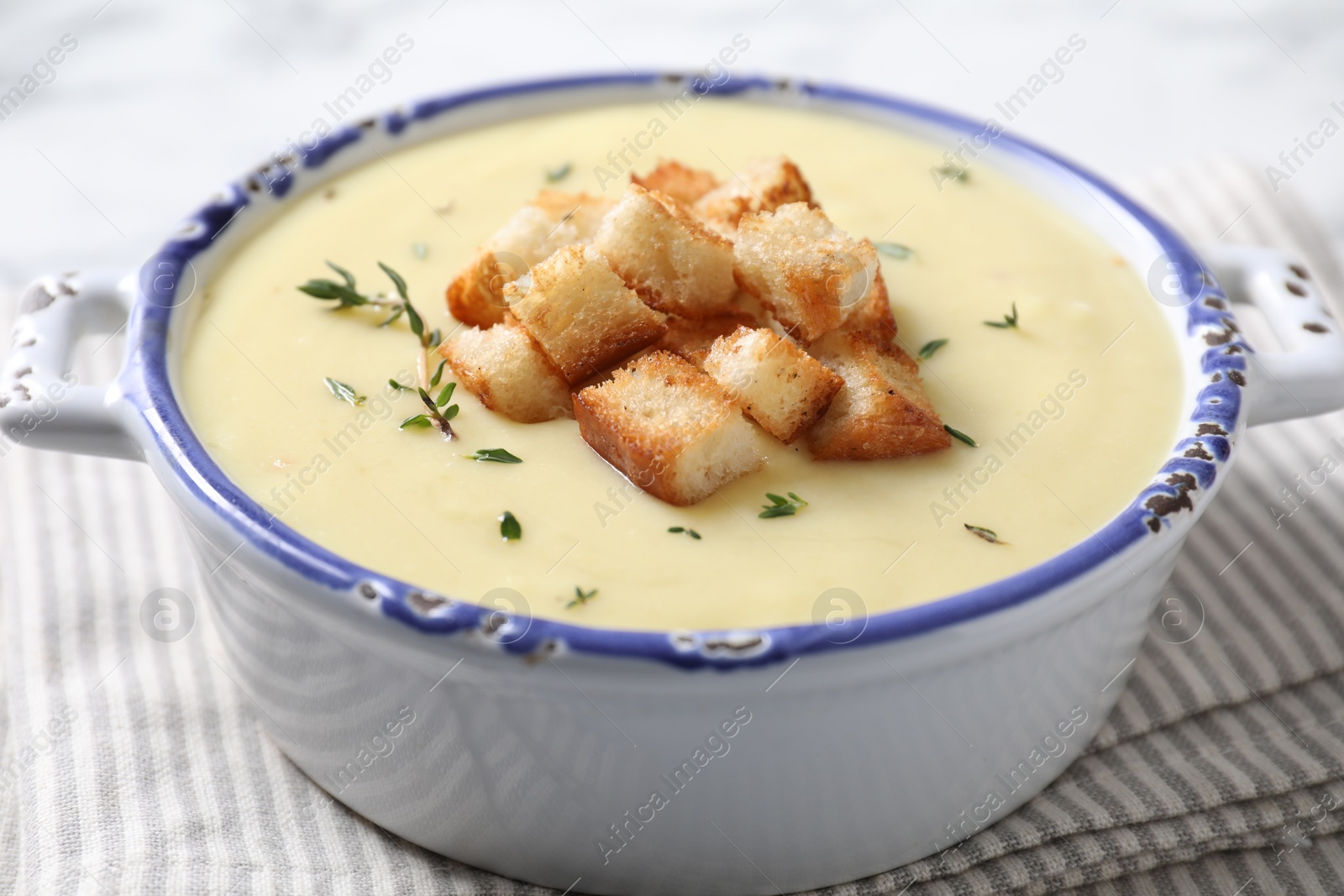 Photo of Tasty potato soup with croutons and rosemary in ceramic pot on white table, closeup