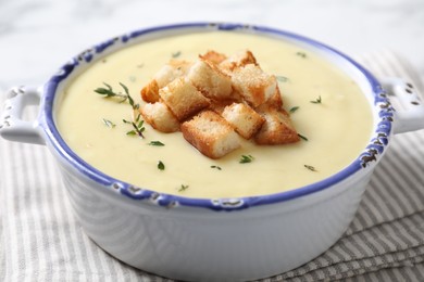 Tasty potato soup with croutons and rosemary in ceramic pot on white table, closeup