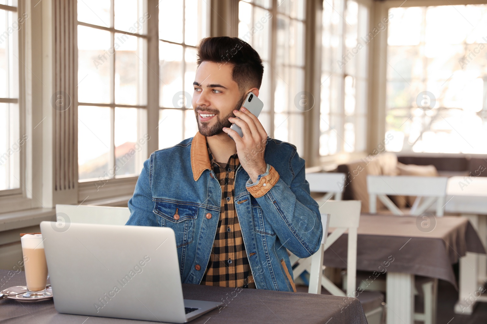 Photo of Young blogger talking on phone at table in cafe