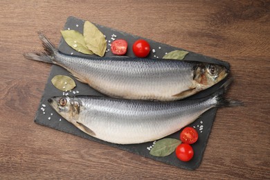 Slate plate with salted herrings, bay leaves and cherry tomatoes on wooden table, top view
