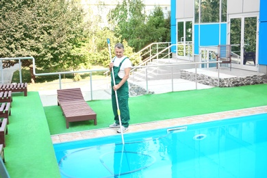 Male worker cleaning outdoor pool with underwater vacuum