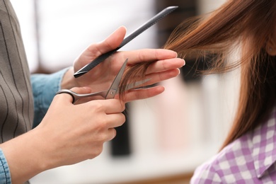 Barber making stylish haircut with professional scissors in beauty salon, closeup