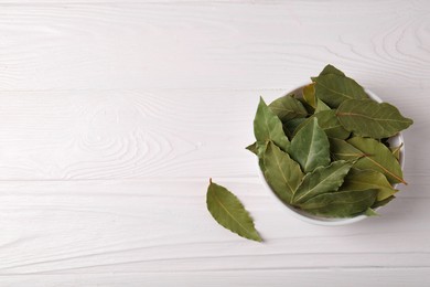 Photo of Dry bay leaves in bowl on white wooden table, flat lay. Space for text