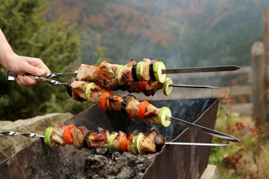 Photo of Woman cooking meat and vegetables on brazier against mountain landscape, closeup