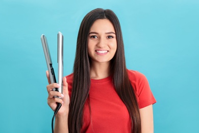 Photo of Young woman with modern hair iron on blue background