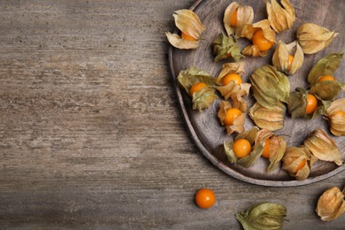 Ripe physalis fruits with dry husk on wooden table, flat lay. Space for text