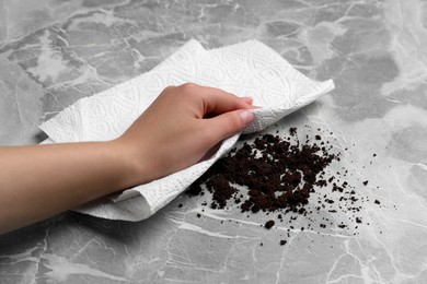Photo of Woman sweeping scattered coffee grounds with paper towel from marble table, closeup