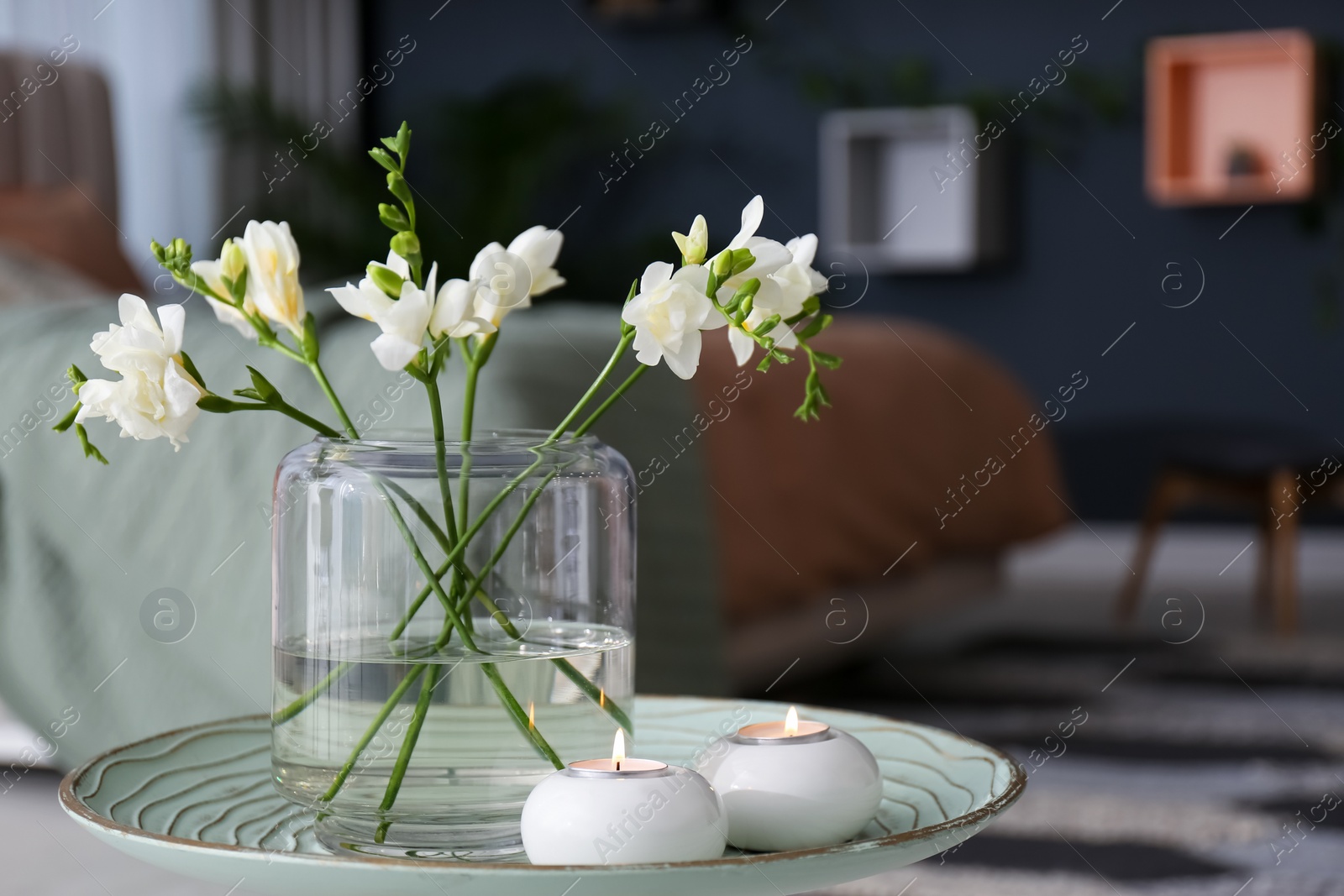 Photo of Vase with beautiful freesia flowers and burning candles on stand in bedroom, space for text. Interior elements