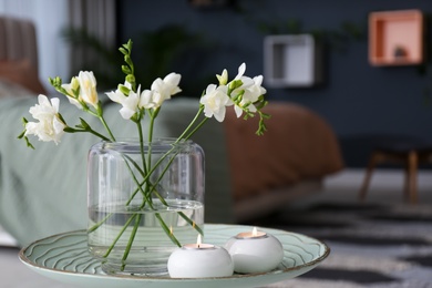 Vase with beautiful freesia flowers and burning candles on stand in bedroom, space for text. Interior elements