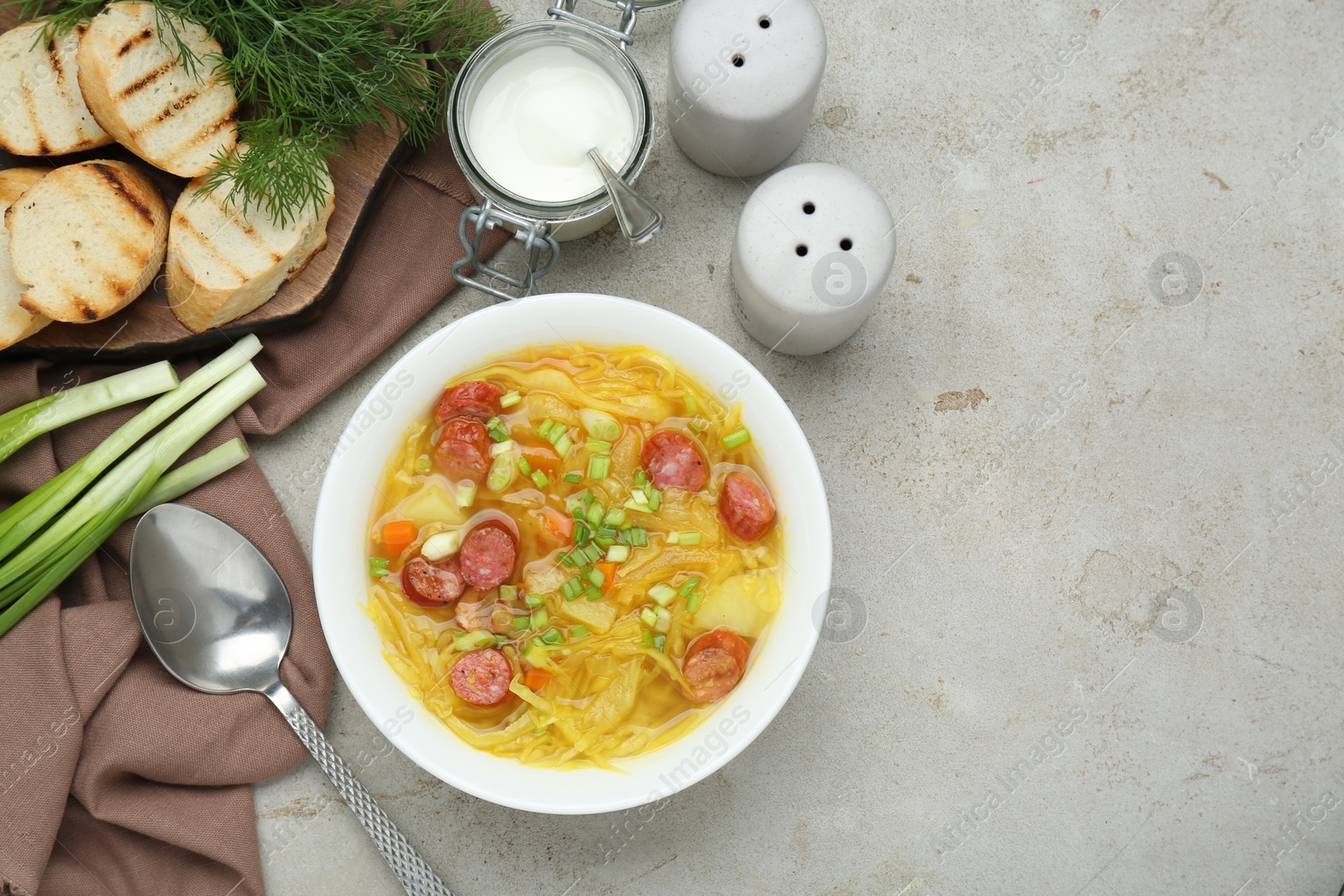Photo of Delicious sauerkraut soup with smoked sausages and green onion served on light grey table, flat lay. Space for text