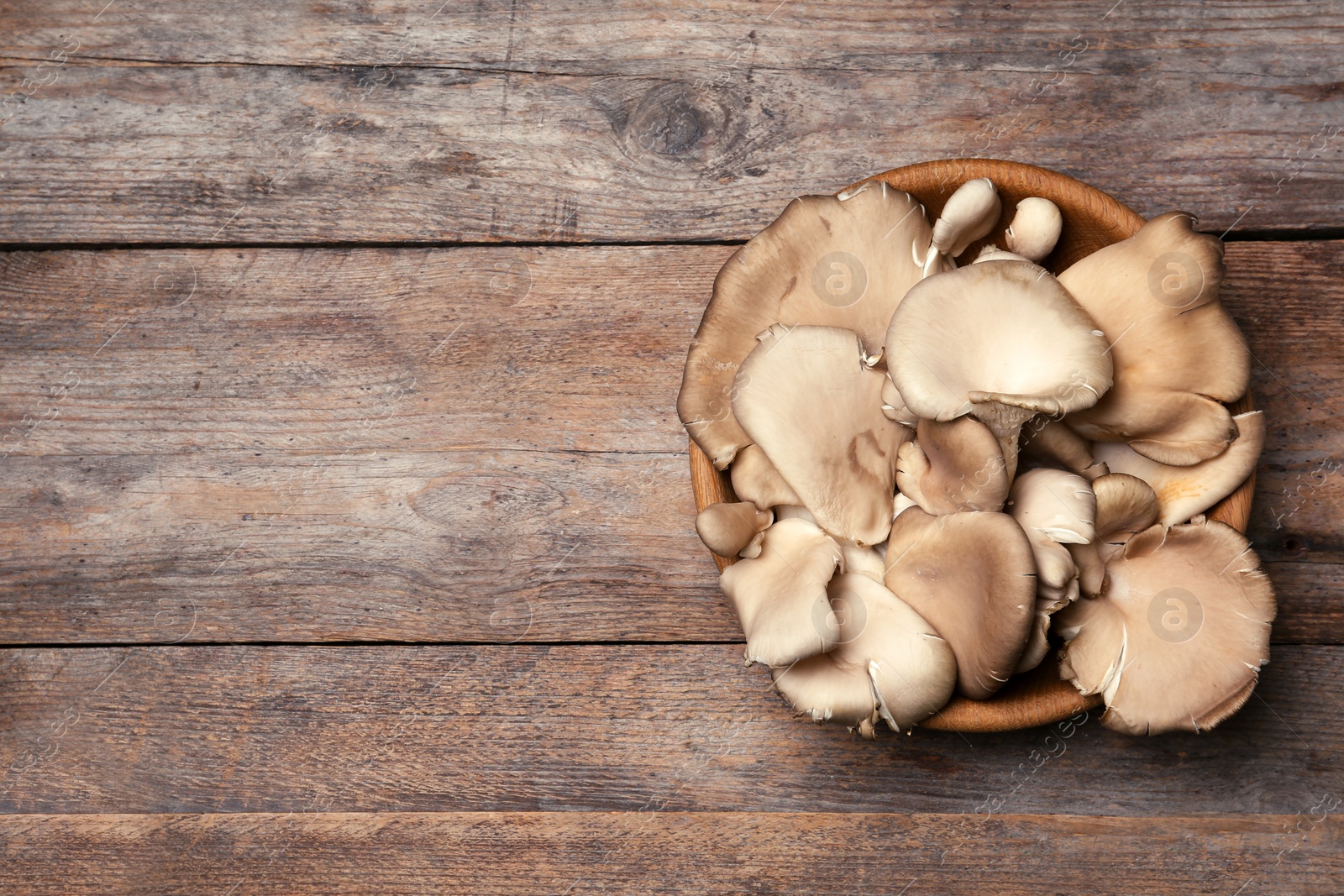 Photo of Bowl of delicious organic oyster mushrooms on wooden background, top view with space for text