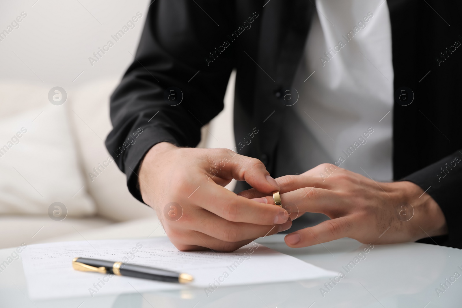 Photo of Man taking off wedding ring at table indoors, closeup. Divorce concept