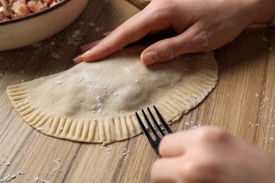 Woman making chebureki with tasty filling at wooden table, closeup