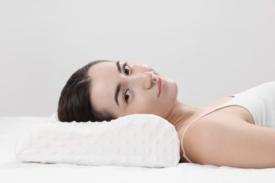 Photo of Woman lying on orthopedic pillow against light grey background