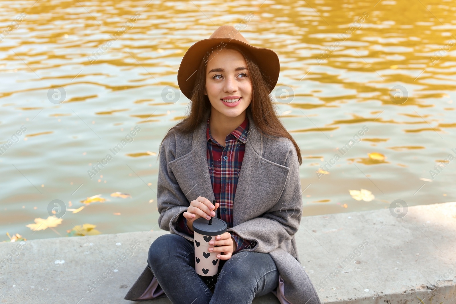 Photo of Portrait of young beautiful woman with drink near pond in park. Autumn walk