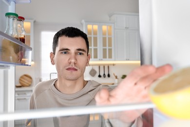 Upset man near empty refrigerator in kitchen, view from inside