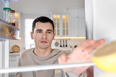 Photo of Upset man near empty refrigerator in kitchen, view from inside