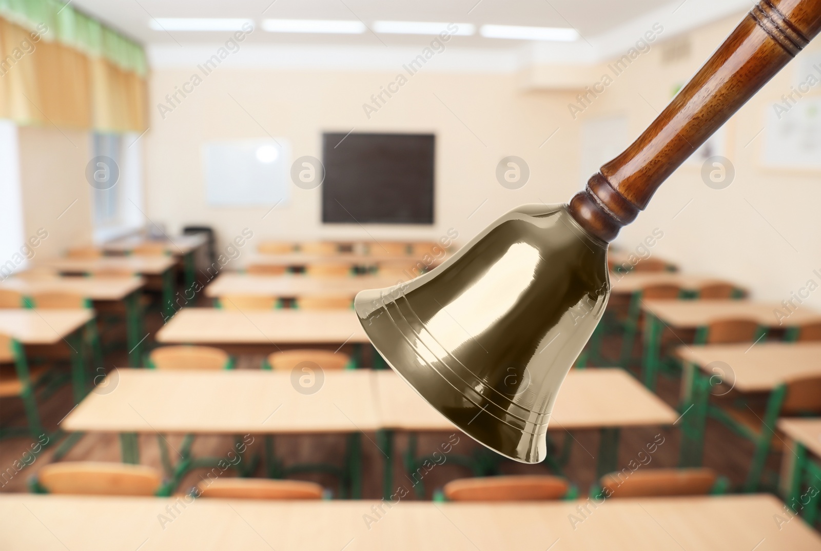 Image of Golden school bell with wooden handle and blurred view of empty classroom