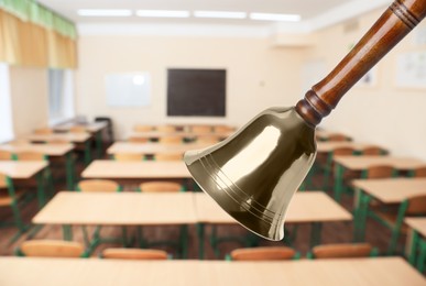 Image of Golden school bell with wooden handle and blurred view of empty classroom