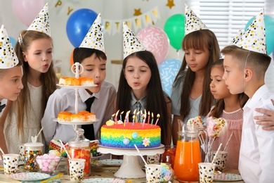 Photo of Happy children blowing out candles on cake at birthday party indoors