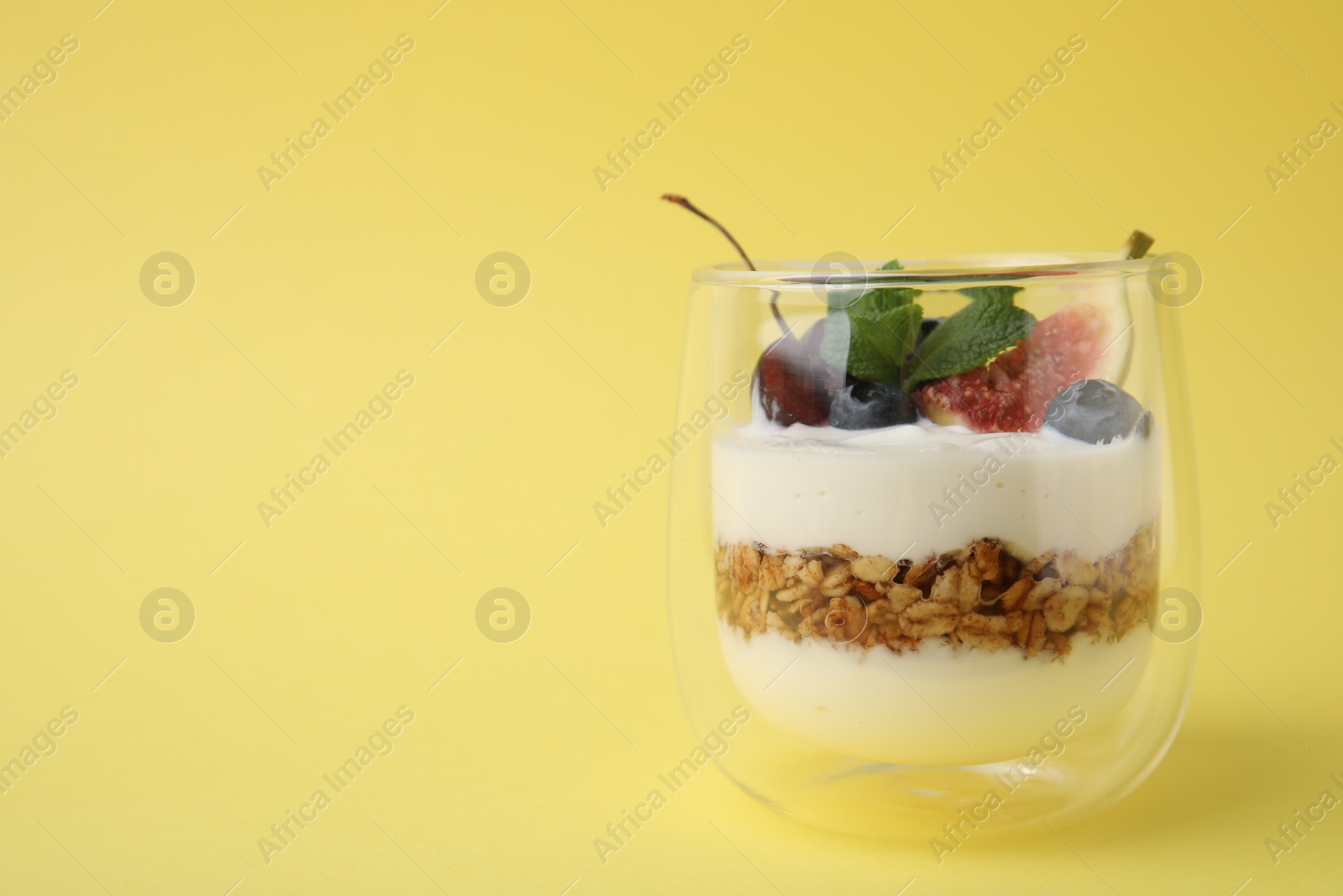 Photo of Glass with yogurt, berries and granola on yellow background. Space for text