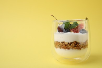 Photo of Glass with yogurt, berries and granola on yellow background. Space for text