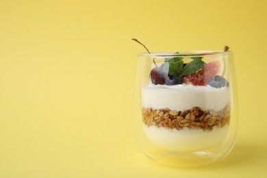 Glass with yogurt, berries and granola on yellow background. Space for text