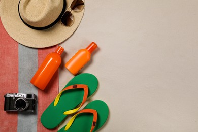 Photo of Beach towel, hat, sunglasses, camera, sunscreen and flip flops on sand, flat lay. Space for text
