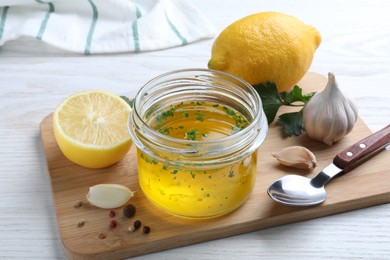 Photo of Jar with lemon sauce and ingredients on white wooden table. Delicious salad dressing