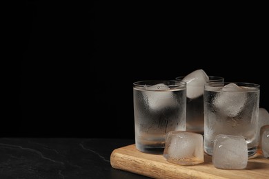 Photo of Shot glasses of vodka with ice cubes on black textured table. Space for text