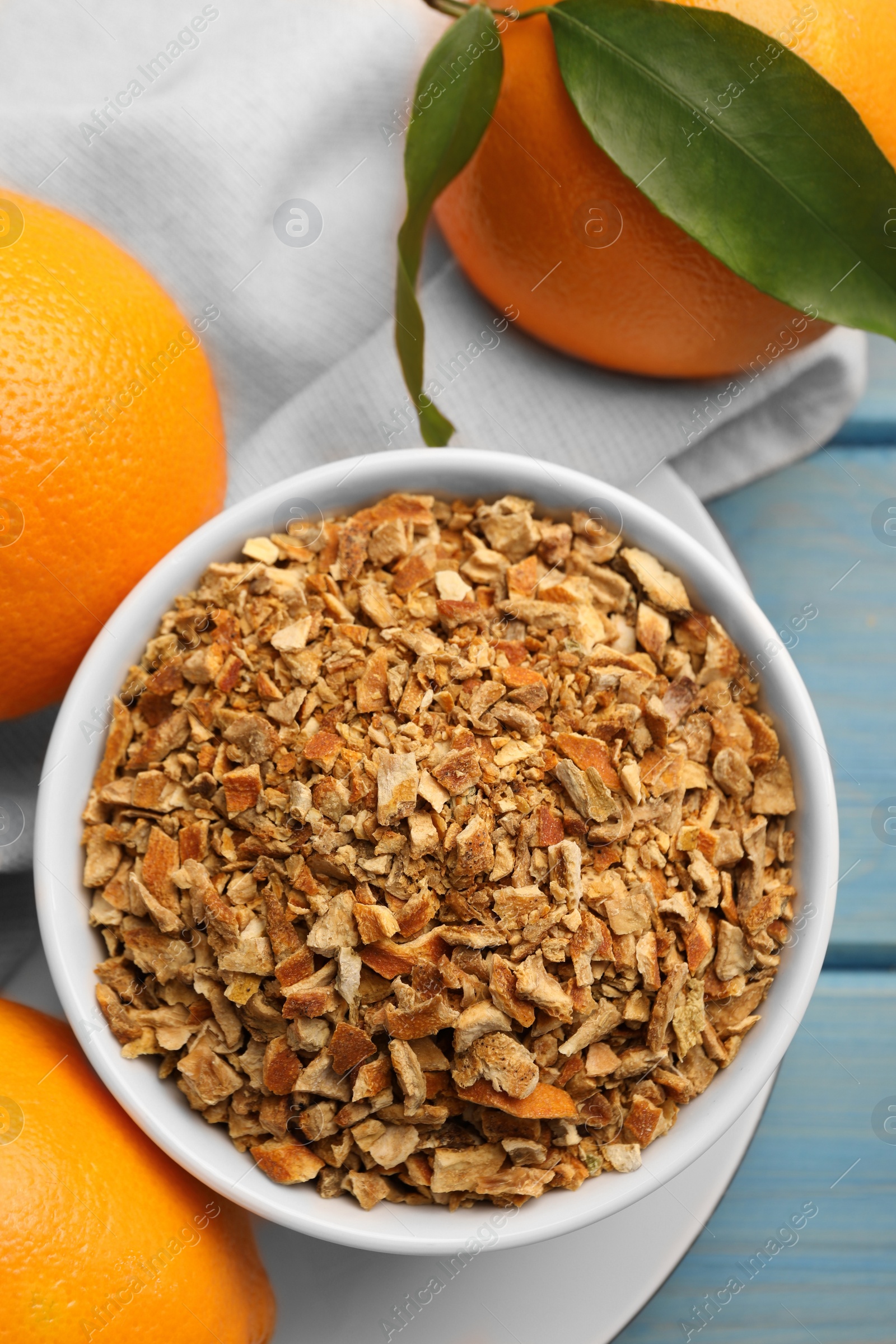 Photo of Bowl of dried orange zest seasoning and fresh fruits on blue wooden table, flat lay