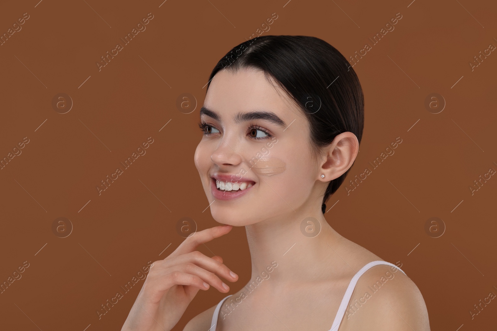 Photo of Teenage girl with swatch of foundation on face against brown background