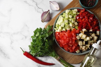 Cooking delicious ratatouille. Fresh ripe vegetables and plate on white marble table, flat lay. Space for text