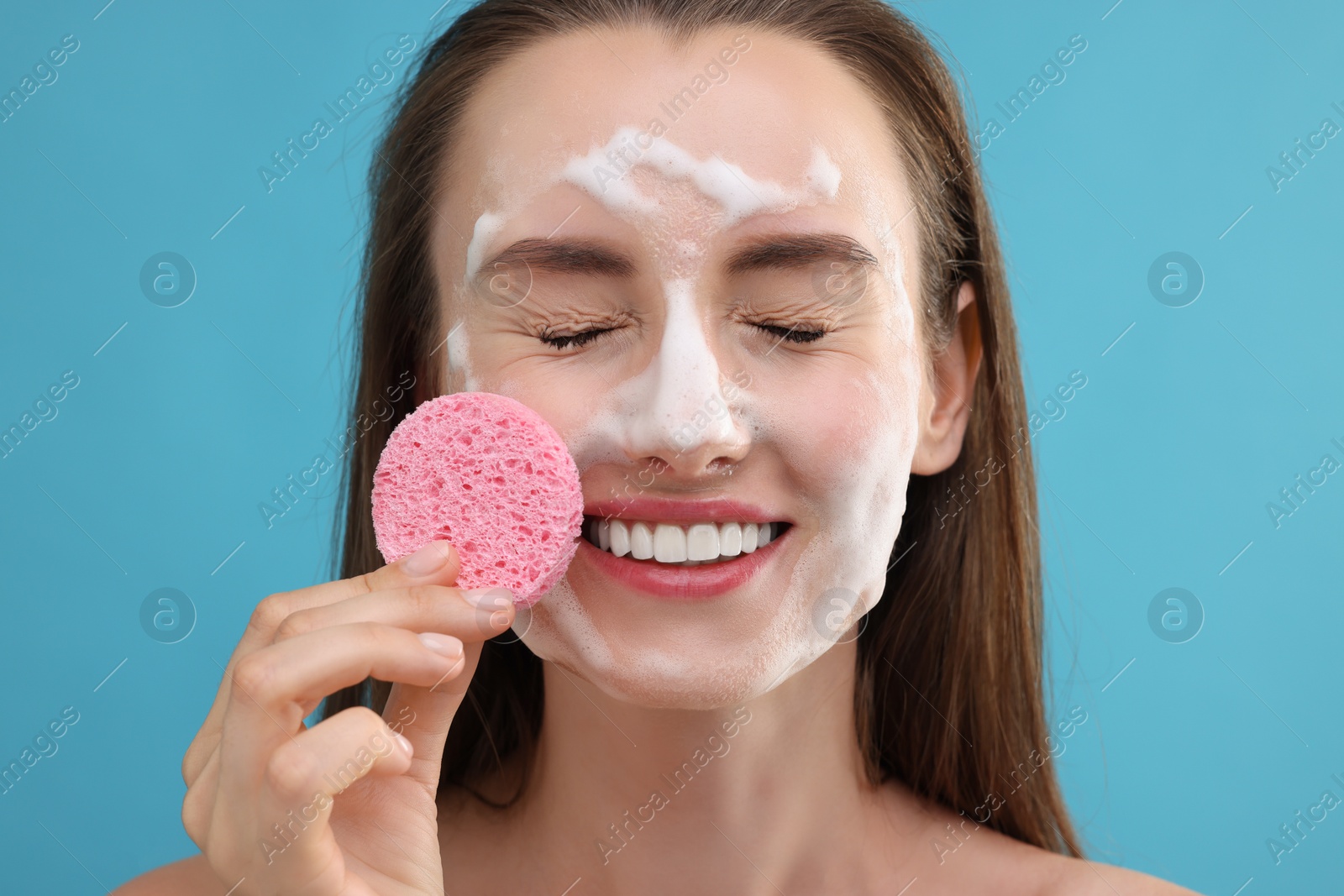 Photo of Happy young woman washing her face with sponge on light blue background