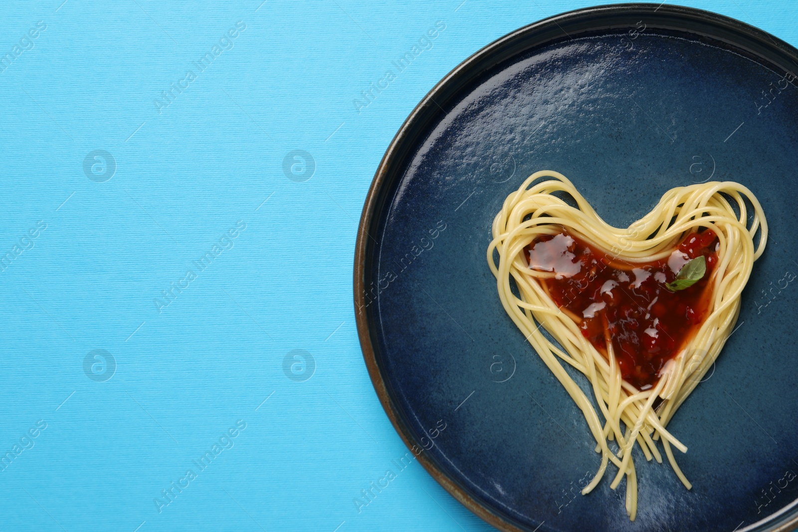 Photo of Heart made with spaghetti and sauce on light blue background, top view. Space for text