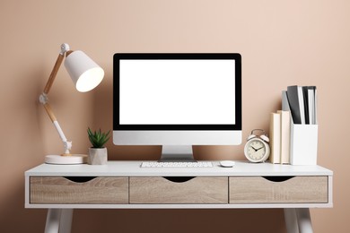 Cozy workspace with computer, lamp, houseplant and stationery on wooden desk